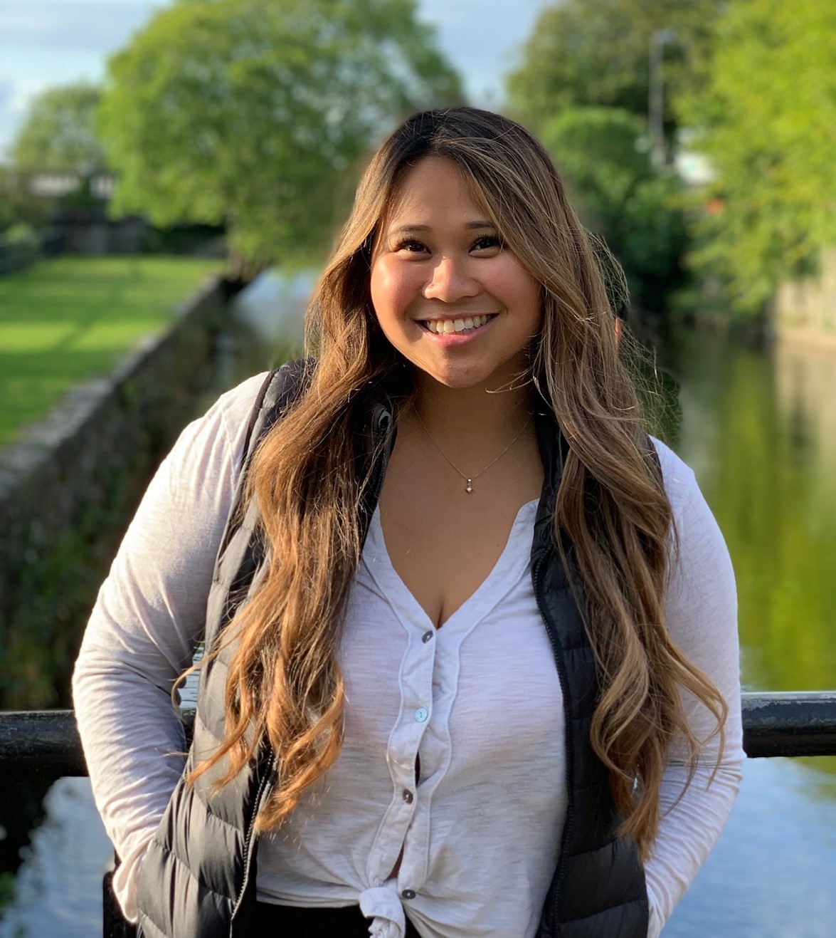 Sharlena, smiling, standing on a bridge over a river